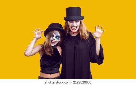 Mother And Child Having Fun On Halloween. Studio Portrait Mum And Daughter In Spooky Costumes. Beautiful Vampire Woman And Little Girl With Catrina Make Up Look At Camera Isolated On Yellow