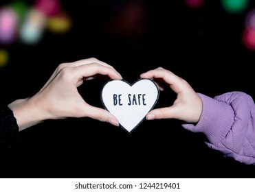 Mother And Child Holding Heart-shaped Pedestrian Safety Reflector With Text Be Safe Outdoors With Dark Background And Bokeh City Street Lights