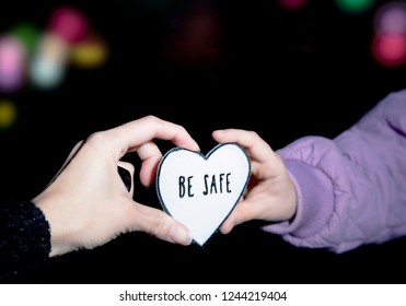 Mother And Child Holding Heart-shaped Pedestrian Safety Reflector With Text Be Safe Outdoors With Dark Background And Bokeh City Street Lights