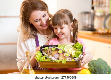 Mother And Child Jolly Look At Prepared Dish Of Fish In Kitchen