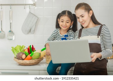 Mother And Child Is Looking At Laptop Computer For Online Cooking Class In Kitchen With Healthy Vegetable In The Background.