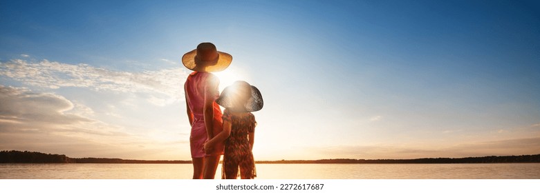Mother and child are looking at seascape at sunset. Family summer vacation at sea concept. Warm rays of sunlight. Back view.