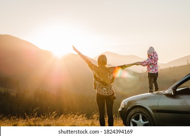 Mother And Child In Mountains On The Sunset Near Car. Mom And Daughter - Tourist Girls. Toward Adventure! Family Enjoying Road Trip On Autumn Vacation. Holiday And Travel Concept. Back View.