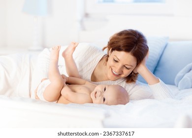 Mother and child on a white bed. Mom and baby boy in diaper playing in sunny bedroom. Parent and little kid relaxing at home. Family having fun together. Bedding and textile for infant nursery. - Powered by Shutterstock