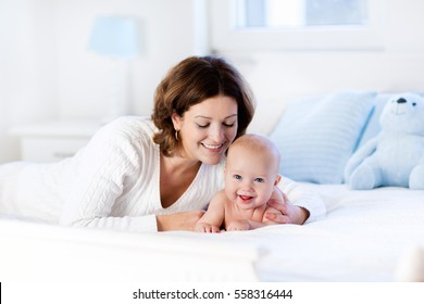 Mother And Child On A White Bed. Mom And Baby Boy In Diaper Playing In Sunny Bedroom. Parent And Little Kid Relaxing At Home. Family Having Fun Together. Bedding And Textile For Infant Nursery