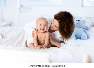 Mother And Child On A White Bed. Mom And Baby Boy In Diaper Playing In Sunny Bedroom. Parent And Little Kid Relaxing At Home. Family Having Fun Together. Bedding And Textile For Infant Nursery