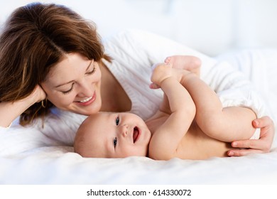 Mother And Child On A White Bed. Mom And Baby Boy In Diaper Playing In Sunny Bedroom. Parent And Little Kid Relaxing At Home. Family Having Fun Together. Bedding And Textile For Infant Nursery.