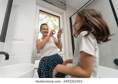 A mother and child playfully splash each other with water from their wet hands after their morning wash in the bathroom. The mom and her son have fun in the bathroom during their morning routine. - Powered by Shutterstock