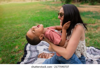 Mother and child playing happily sitting on the grass in an outdoor park, the mother tickles her child