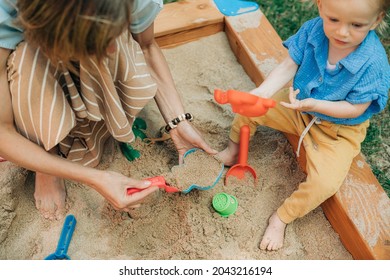 Mother And Child Playing Together In Sandpit. Woman Playing With Little Daughter On Playground Outdoors. Childhood And Parenthood Concept