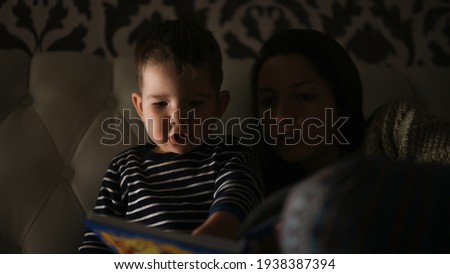 Mother with child read a book in the dark, before bedtime . High quality photo
