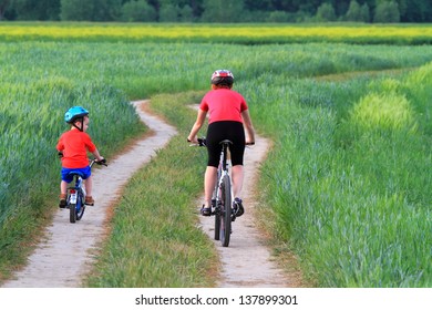 Mother and child riding bikes together on a green field
