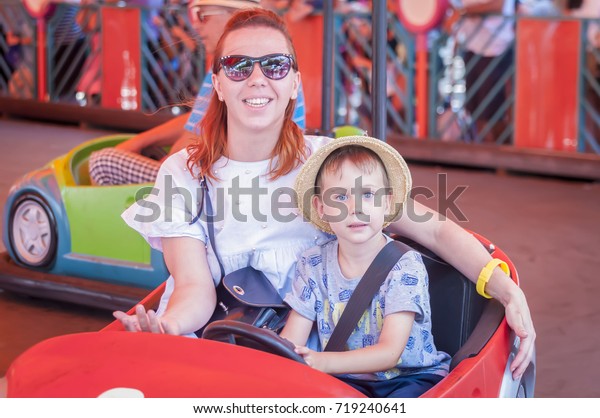 Mother and child riding a car in the\
attraction park. Amusement Park Bumper\
car