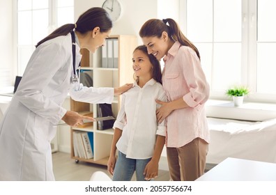 Mother And Child Seeing Doctor Together. Smiling Pediatrician Welcoming Patient At Her Office. Friendly General Practitioner Talking To Teen Girl Who Came With Her Mom For Health Checkup To The Clinic