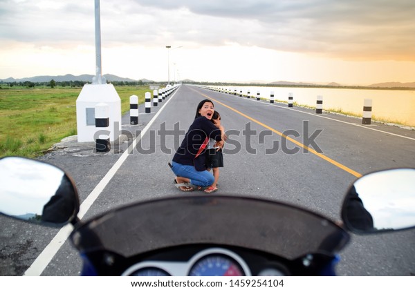 Mother and child are shocked that a\
motorcycle is about to crash on the road. Mother and child are hit\
by a motorcycle on the road. Concepts for accidents and safety.\
Front view motorcycle.\
