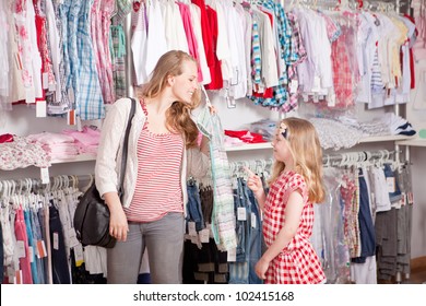 Mother And Child Shopping Choosing Dress In Clothes Shop