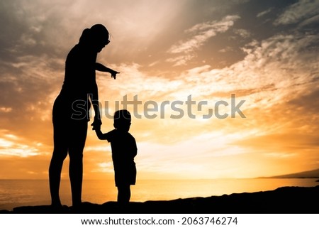 Mother and child silhouette by the sea at sunset.
