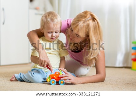 mother and child son playing with toy cars on floor at home