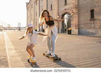Mother and child spending their free time skateboarding outdoors. Happy family spending leisure time together.