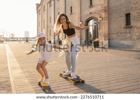 Mother and child spending their free time skateboarding outdoors. Happy family spending leisure time together.