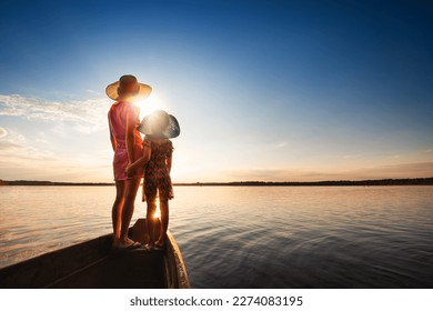 Mother and child swim in boat with seascape in background at sunset. Mother hugs her child. Back view. - Powered by Shutterstock