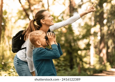 Mother child together hiking in the forest looking through binoculars bird watching exploring learning about nature, family adventure 