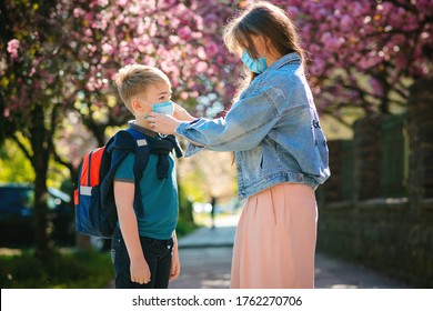 Mother And Child Wearing Face Mask Going To School During Coronavirus Outbreak. Safety Mask For Illness Prevention. Mom And Kid At School During Covid 19 Pandemic. Woman Puts On Kid Face Mask.