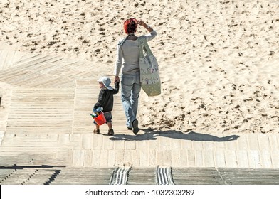 Mother With Child Wearing A White Cap Walking To The Beach With On Her Shoulder A Big Bag