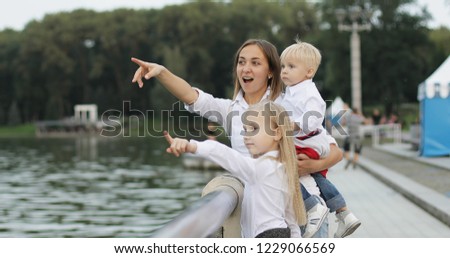 Mother with children admire the view of the lake in the summer. A young woman with the eldest daughter holds a small son in her arms. A happy family.
