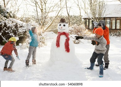 Mother And Children Building Snowman In Garden