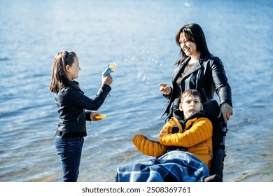 Mother and children enjoying outdoor time by the lake, inclusive family activities, child in wheelchair, sibling blowing bubbles, disability inclusion, family bonding.

 - Powered by Shutterstock