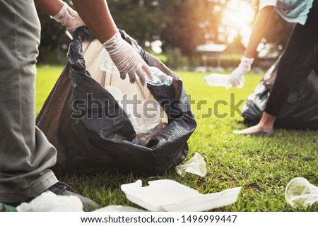 mother and children keeping garbage plastic bottle into black bag at park in morning light