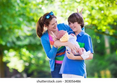 Mother and children play in a park. Young mom with two sons, newborn and teenager boy. Siblings with big age difference. Brothers with large age gap. Teen kid holding new baby. Parents and kids fun.