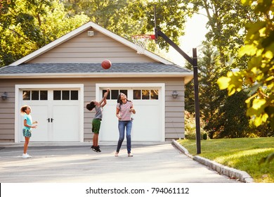 Mother And Children Playing Basketball On Driveway At Home