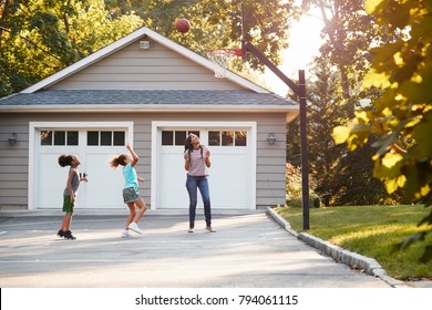 Mother And Children Playing Basketball On Driveway At Home