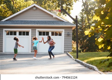 Mother And Children Playing Basketball On Driveway At Home