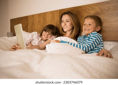 Mother and children using digital tablet in bed