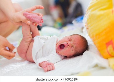 Mother cleaning up her yawning newborn baby's buttocks with wet hankies.