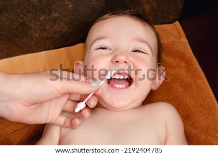 A mother cleans her nose with a cotton swab to a happy toddler baby boy. Mom cleans the nostrils of a smiling child. Kid age one year