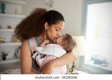 Mother Cuddling Baby Daughter At Home In Front Of Window