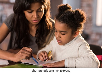 Mother And Cute Little Daughter Sitting At Table And Doing Homework Together At Home, Homework Help Concept