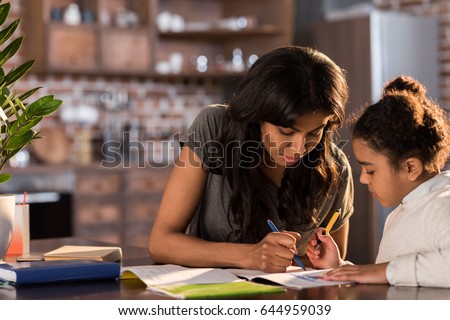 Mother and cute little daughter sitting at table and doing homework together at home, homework help concept