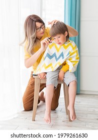 Mother Cuts Her Son's Hair By Herself. Little Boy Sits, Covered With Cloth. New Normal In Case Of Coronavirus COVID-19 Quarantine And Lockdown. Beauty And Self Care At Home Lifestyle.