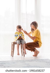 Mother Cuts Her Son's Hair By Herself. Little Boy Sits, Covered With Cloth. New Normal In Case Of Coronavirus COVID-19 Quarantine And Lockdown. Beauty And Self Care At Home Lifestyle.