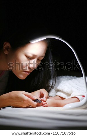 Mother cutting toenails of her baby on the bed after baby sleep at night.