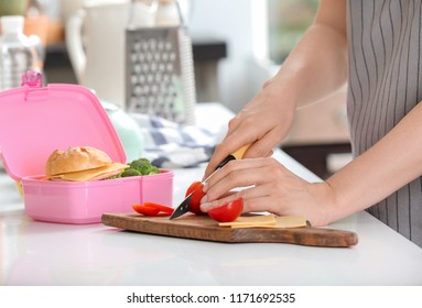 Mother cutting tomato for school lunch at table in kitchen