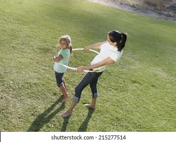 Mother and daughter (6-8) playing with hula hoop on grass in park, smiling, side view, elevated view - Powered by Shutterstock