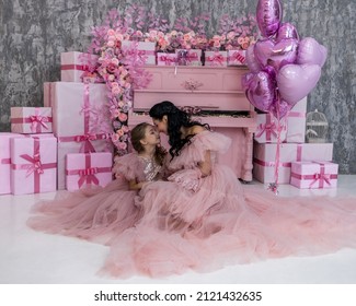 mother and daughter are beautiful in lush, airy pink dresses, near a pink piano, a piano with a huge number of flowers, a lot of flowers, in a festive mood they congratulate everyone on Valentine's Da