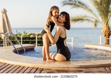 Mother and daughter in black bikini are sitting at the pool edge and enjoying summer vacation time while looking at the camera. Happy child and woman playing in swimming pool. Summer vacation concept - Powered by Shutterstock