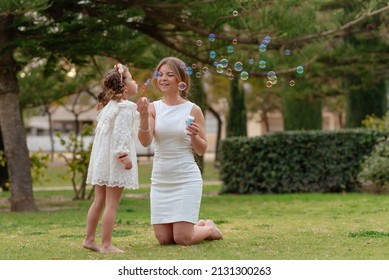 Mother and daughter blow soap bubbles outdoors.
